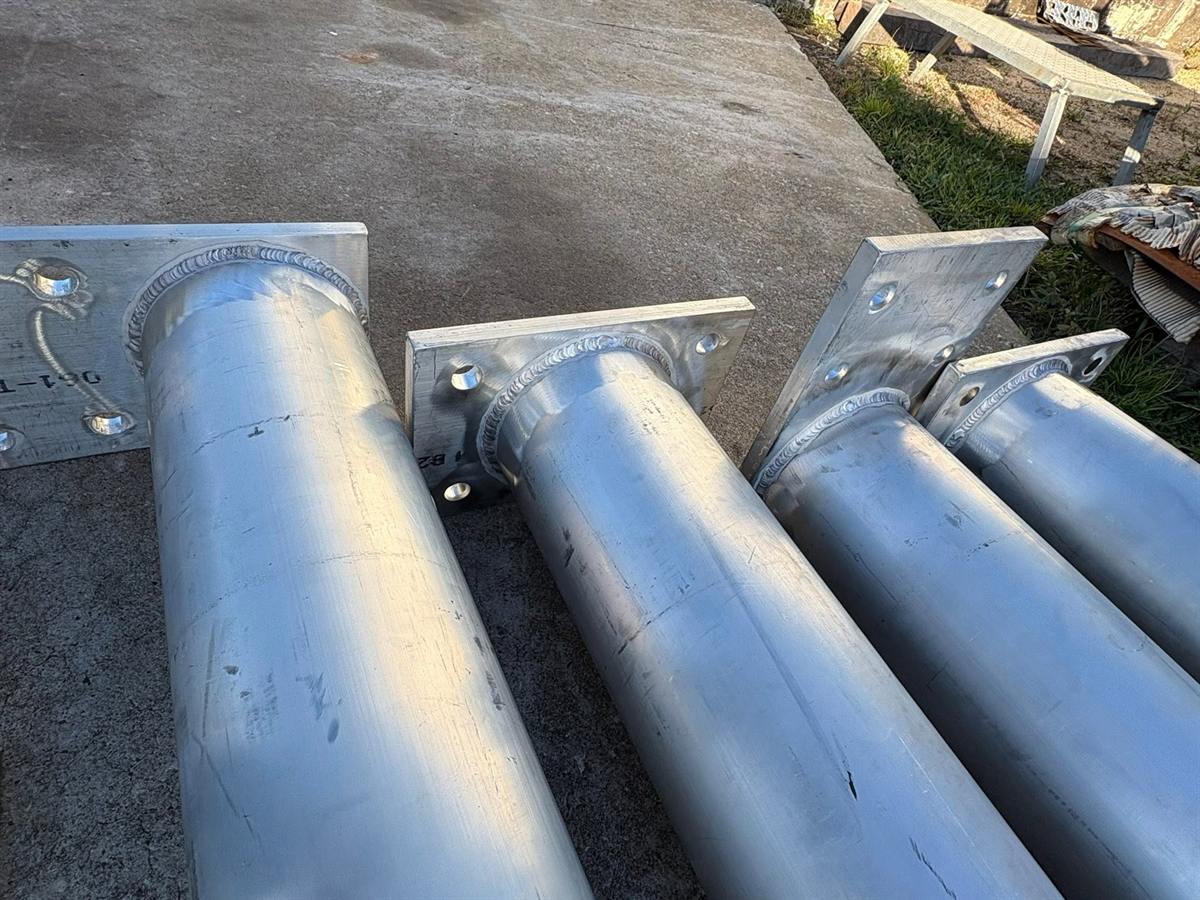 Aluminum posts with welded square base plates and gussets lined up on a concrete floor