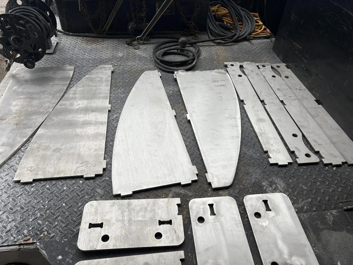 CNC plasma-cut steel plate parts with slots and holes laid out on the shop floor