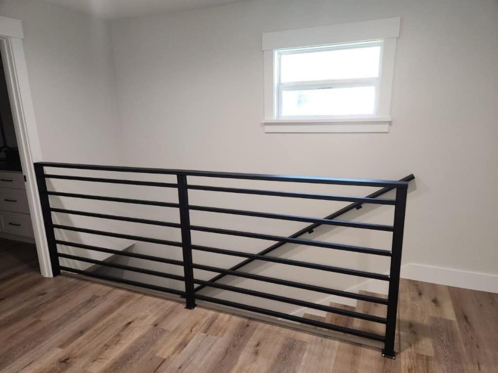 Black horizontal-bar steel railing around an interior stair opening