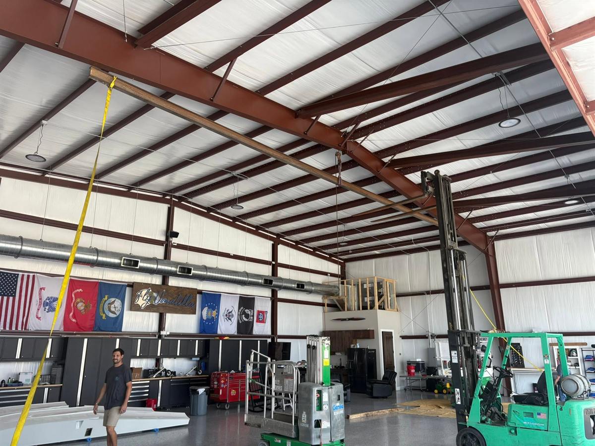 Wide view inside a large metal building used as a fabrication shop, with flags on the back wall